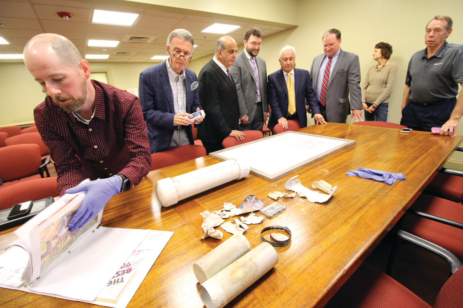CAPSULE AND ITS CONTENTS: Marc Berman, who was a student at Rhodes School, looks through drawings of the school playground where the time capsule, seen in front of him, was buried 32 years ago. With him are those who gathered for the opening of the capsule Thursday morning.